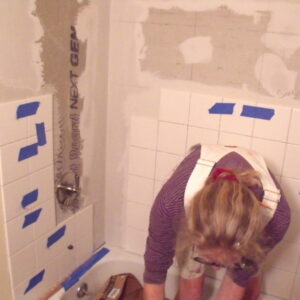 Susan Connery applying tile to bathroom shower.